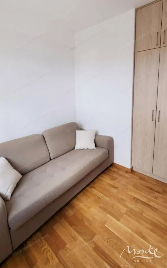 Manja dnevna soba sa bež kaučem i drvenim ormarom.