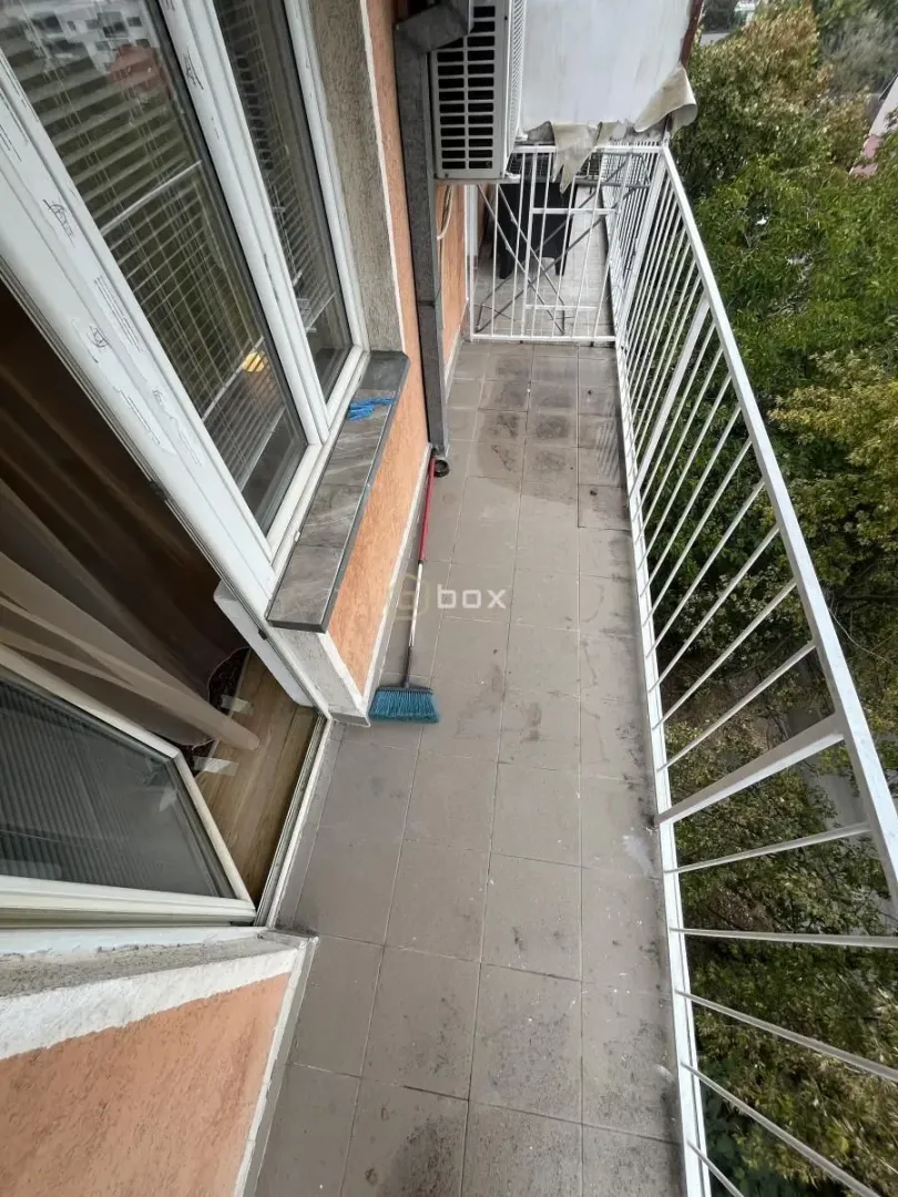 Dugi popločani balkon sa belom ogradom i pogledom na zelenilo.