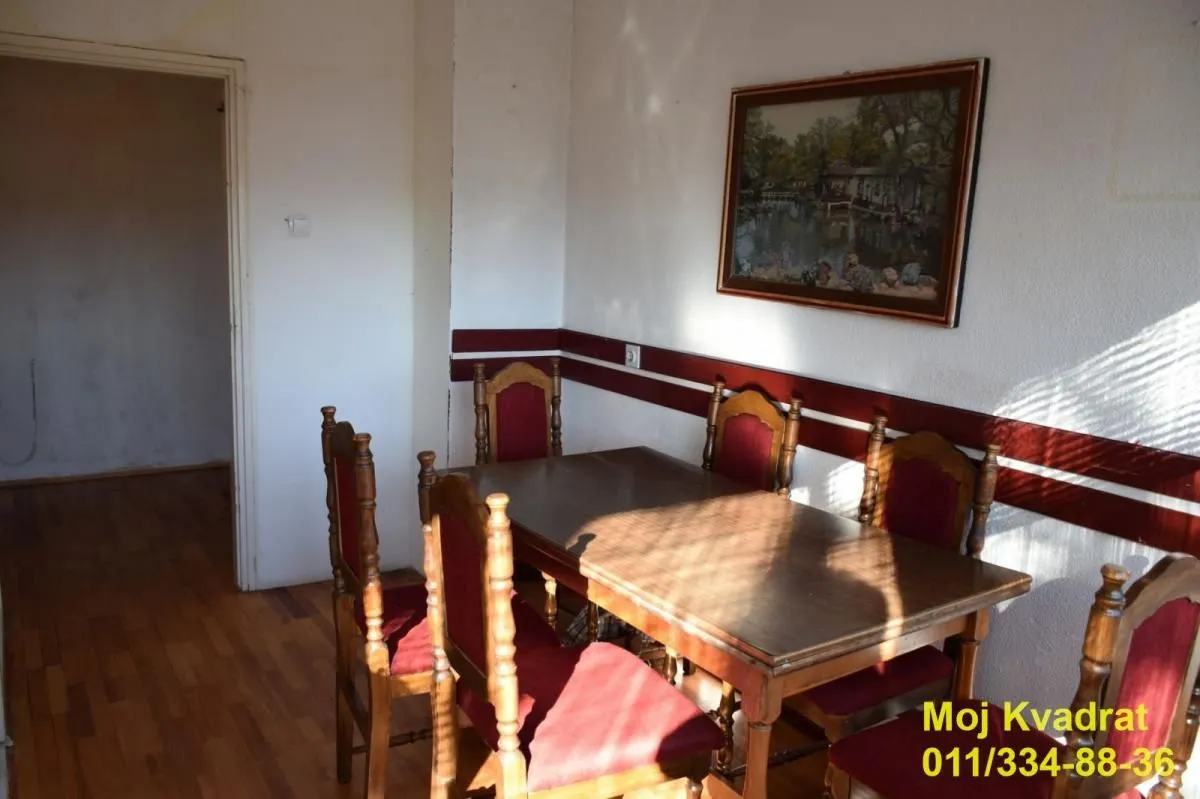 Trpezarija sa drvenim stolom i stolicama, i slikom na zidu.