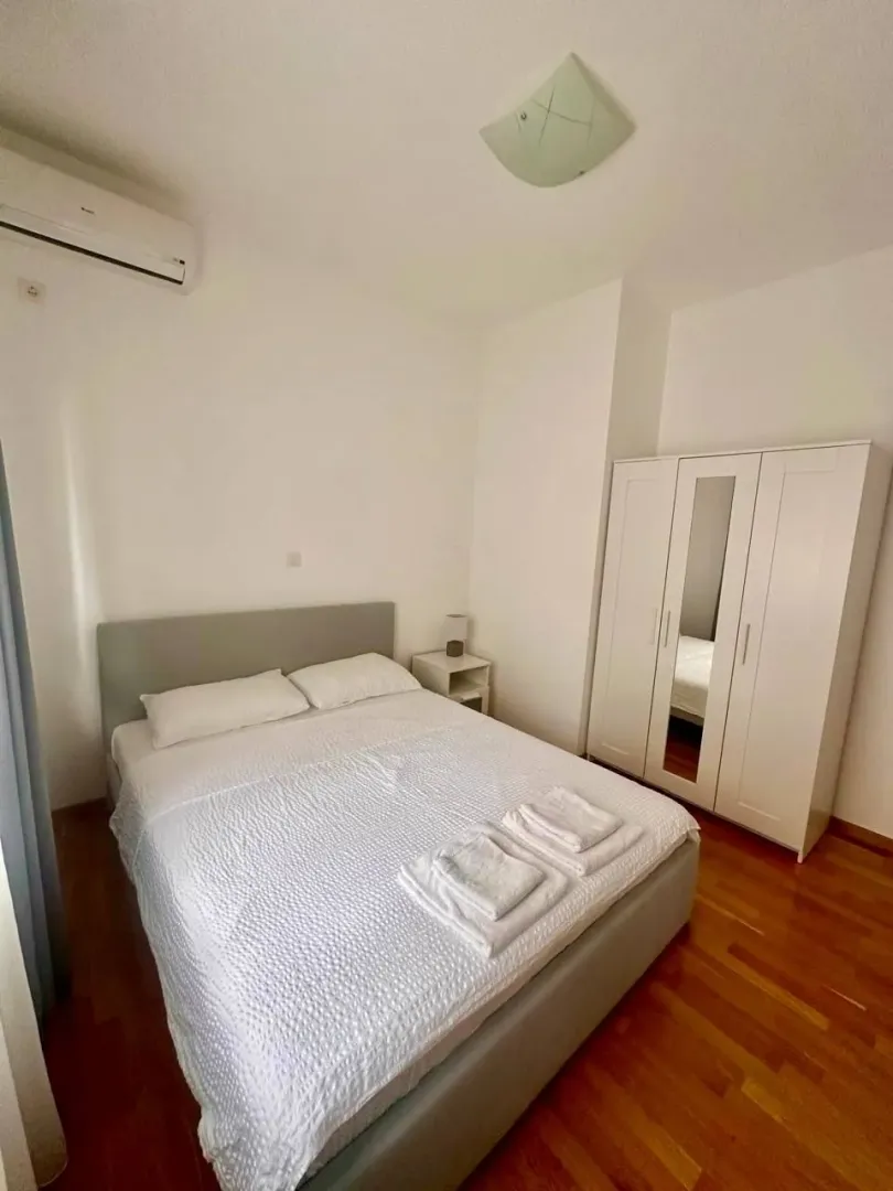 Svijetla spavaća soba sa bračnim krevetom, bijelim garderoberom i drvenim podom.