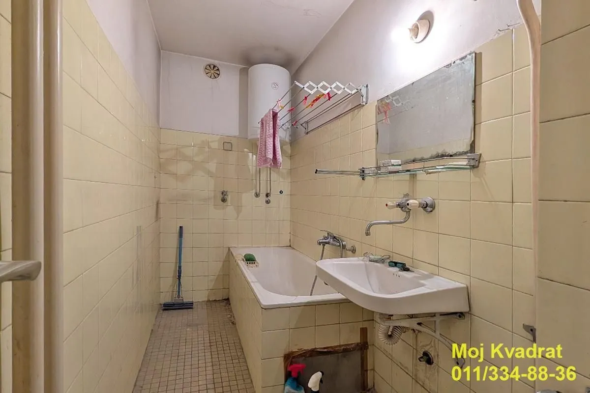 Starije opremljeno kupatilo sa kadom, umivaonikom i bojlerom.