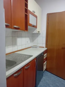 Kuhinja sa drvenim elementima, radnom površinom i ugrađenom mašinom za suđe. - image 17