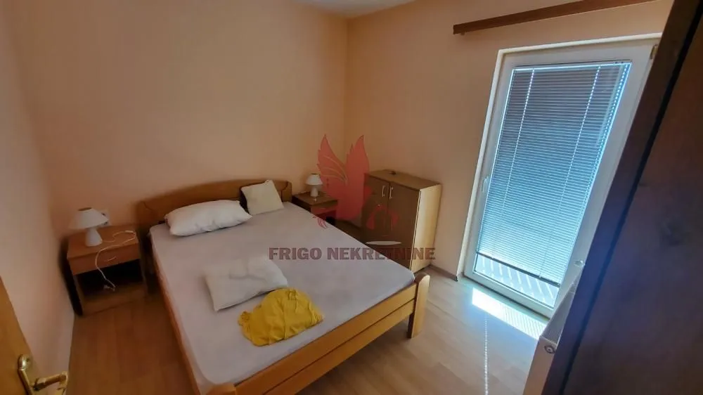 Nameštena spavaća soba sa bračnim krevetom, noćnim stočićima i izlazom na terasu.