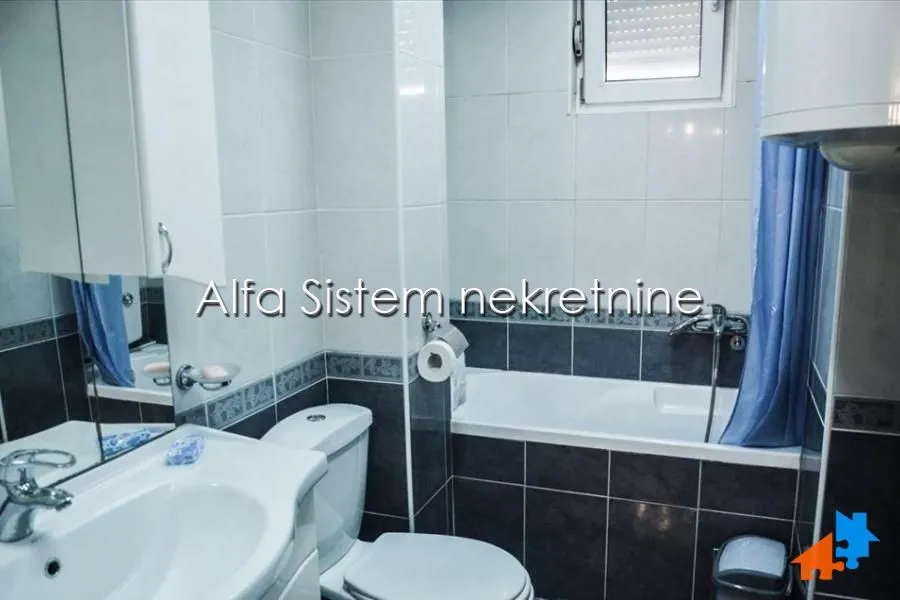 A compact bathroom featuring a bathtub, sink, and toilet, tiled with ceramic tiles.