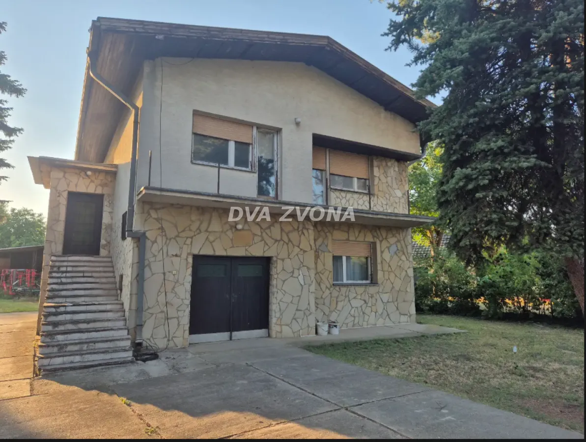 Prednji pogled na spratnu kuću sa kamenom fasadom, garažom i stepeništem.