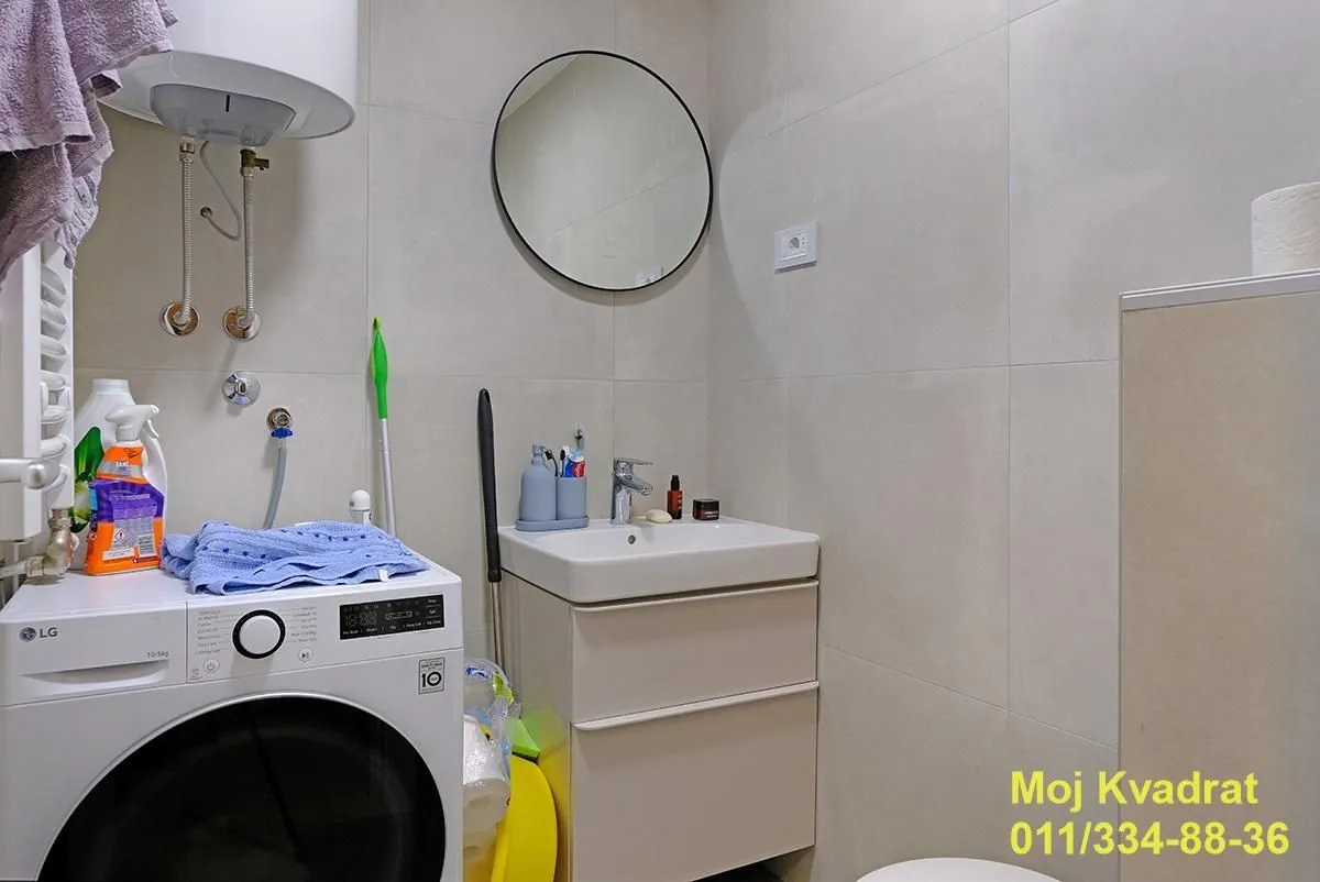 Kupatilo opremljeno umivaonikom, ogledalom i mašinom za veš.