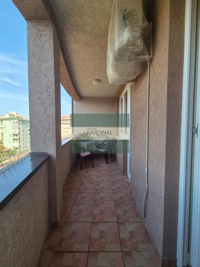 Natkriveni balkon sa popločanim podom i garniturom za sedenje.