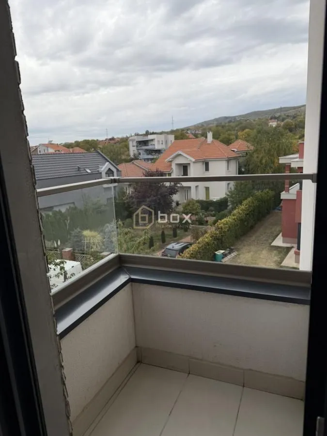 Manji balkon sa staklenom ogradom i pogledom na okolno naselje.