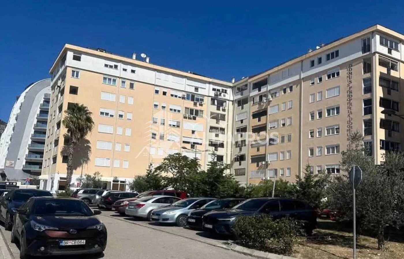 Pogled na spoljašnjost stambene zgrade sa parkingom.