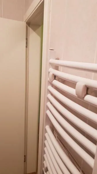 Beli radijator za peškire montiran na zid u kupatilu.