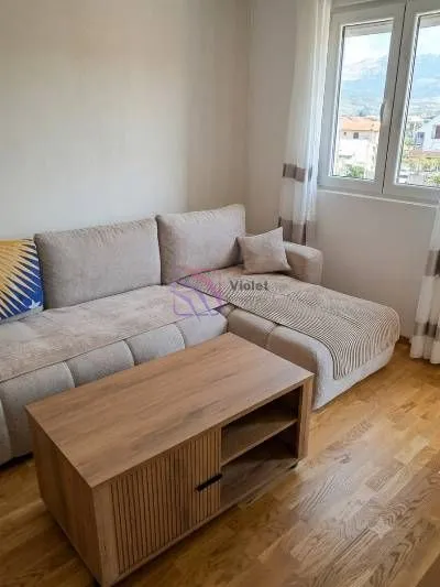 Dnevna soba sa ugaonom garniturom i drvenim stočićem pored prozora.