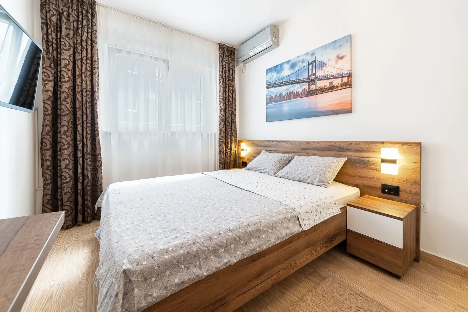 Furnished bedroom with a double bed, bedside tables and a wall-mounted TV.