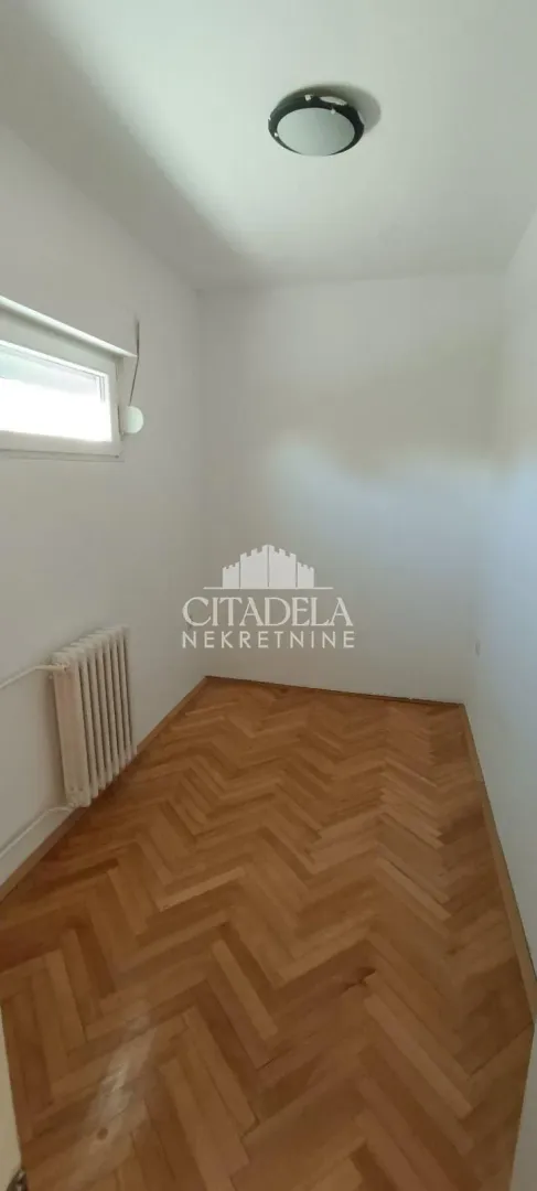 Prazna soba sa parketom i belim zidovima.