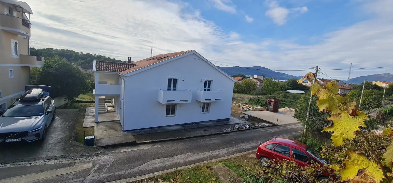 Pogled sa visine na spoljašnjost bijele kuće sa balkonom i dvorištem.