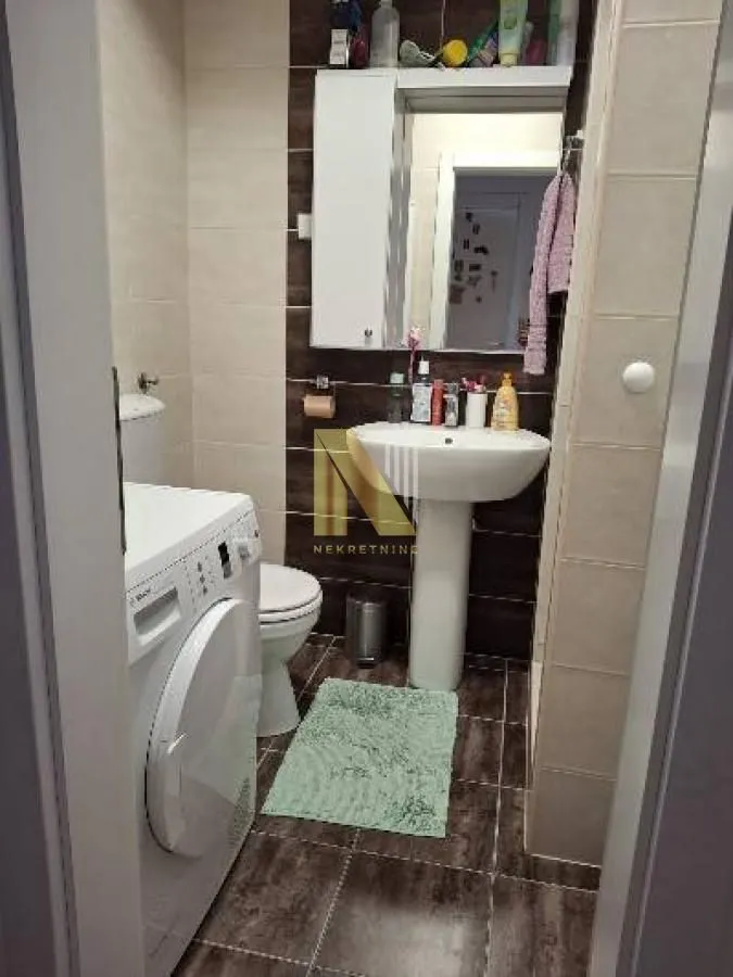 Manje kupatilo sa umivaonikom, WC šoljom, tuš kabinom i veš mašinom.