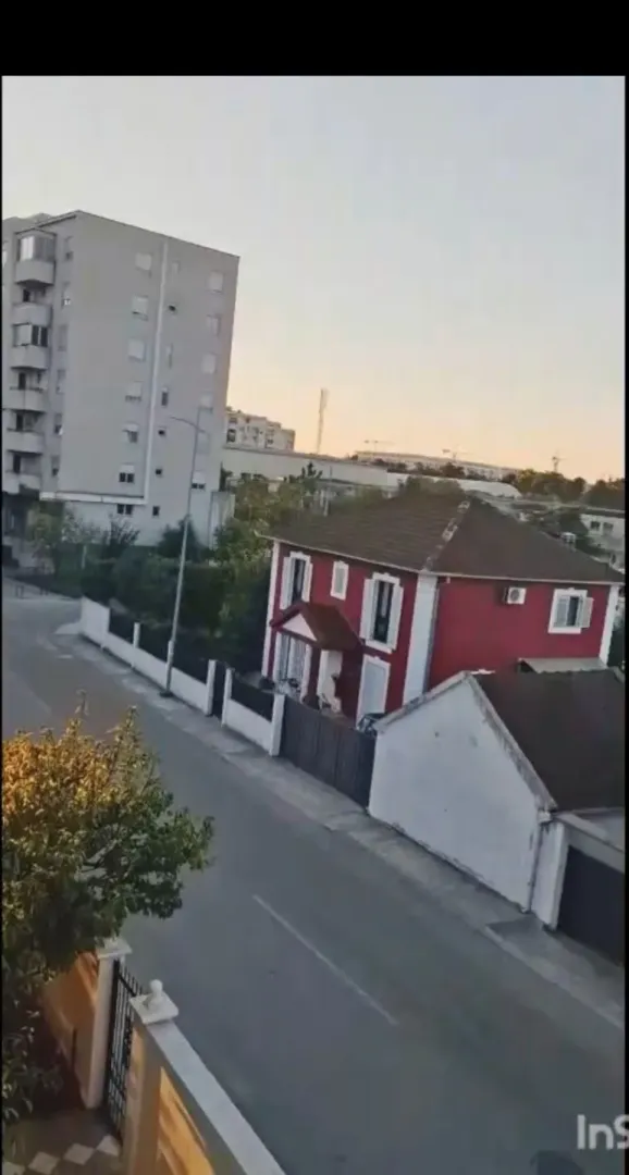 Pogled na ulicu sa crvenom kućom i višespratnom zgradom u pozadini.