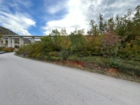 Asfaltni put pored parcele sa rastinjem i pogledom na most u pozadini. - image 3