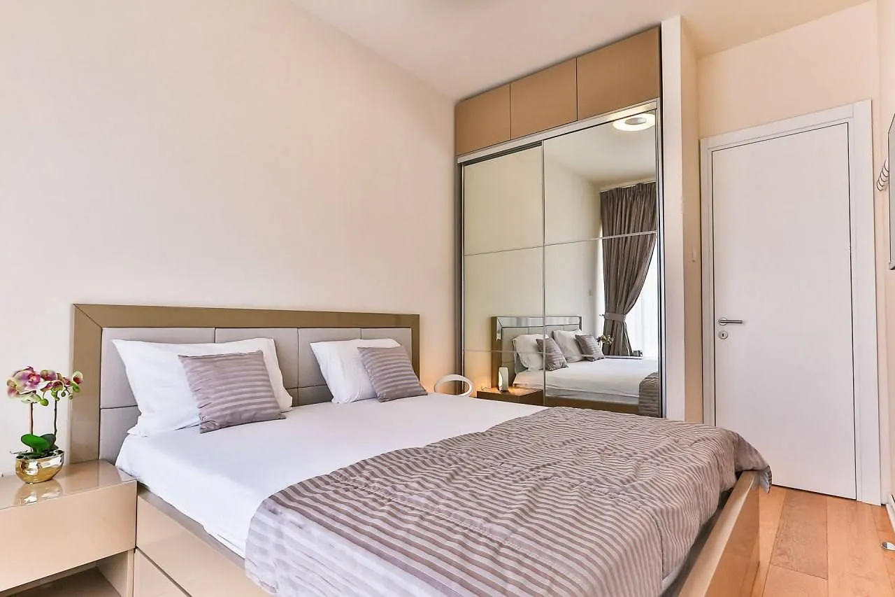 Furnished bedroom with a double bed, large mirrored wardrobe, and a white door.