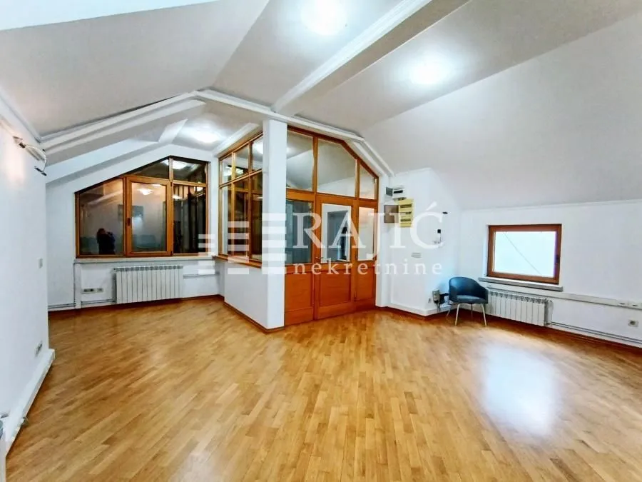 Spacious empty room with wooden flooring and sloped ceiling.