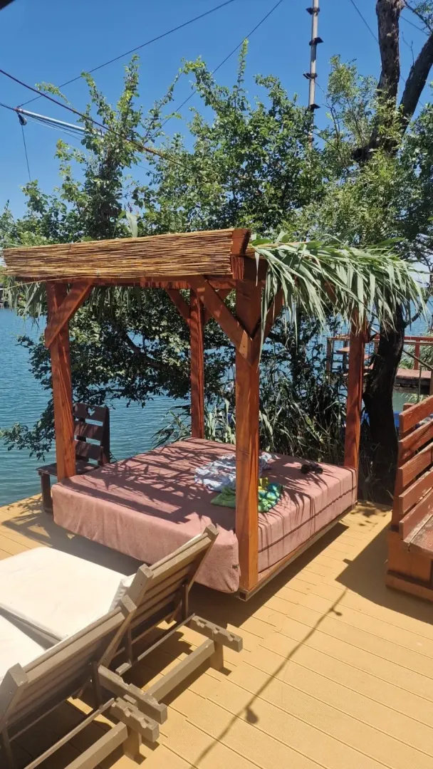 Drvena sjenica sa ležaljkom na terasi pored vode.