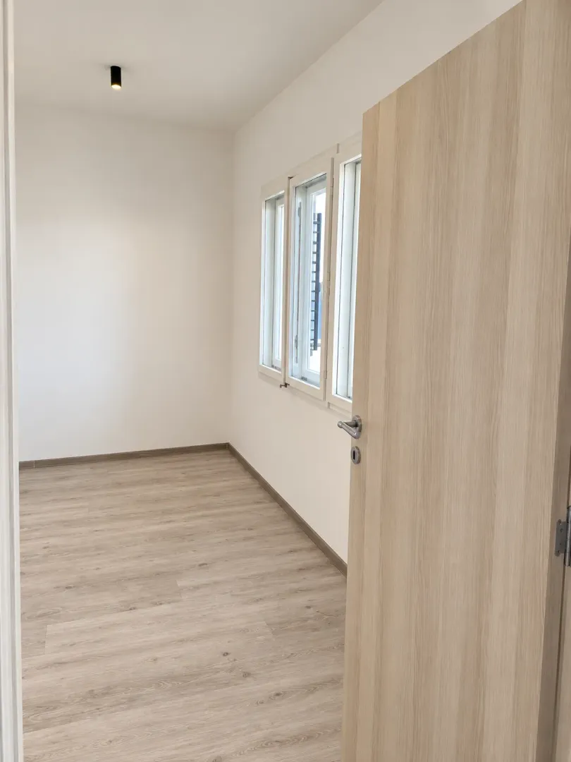 Empty room with light wooden flooring, white walls, and three windows.