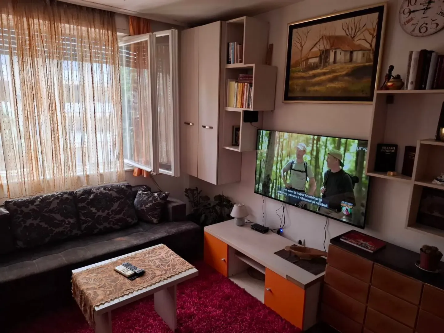 Dnevna soba sa garniturom za sjedenje, televizorom i police na zidu.