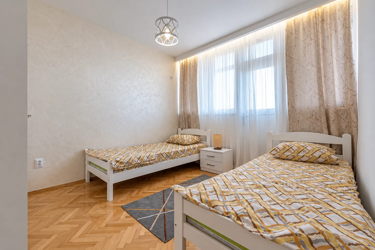 Bedroom with two single beds and a window with light curtains.
