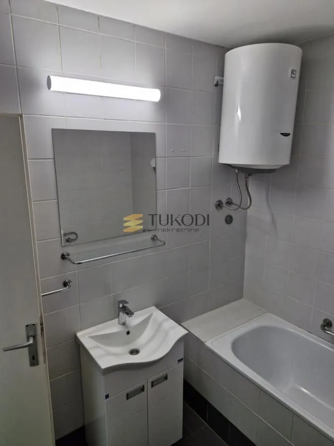 Manje kupatilo sa belim pločicama, umivaonikom i kadom.