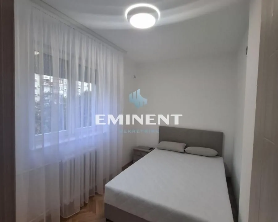 Small bedroom with a double bed and a window covered with a white curtain.