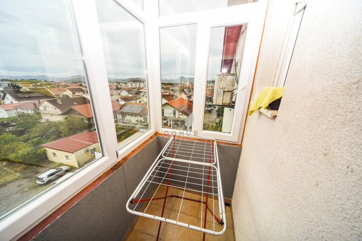 Zastakljeni balkon sa stalkom za sušenje veša i pogledom na naselje.