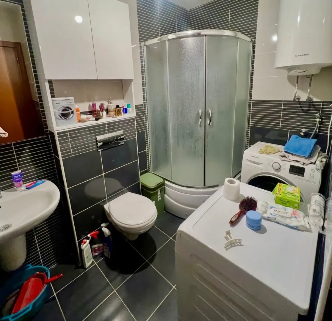 Compact bathroom with a shower cabin, washbasin, toilet, and washing machine.