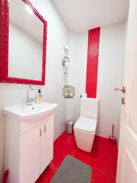 Bathroom equipped with a washbasin, toilet bowl, and a mirror with red details. - image 8