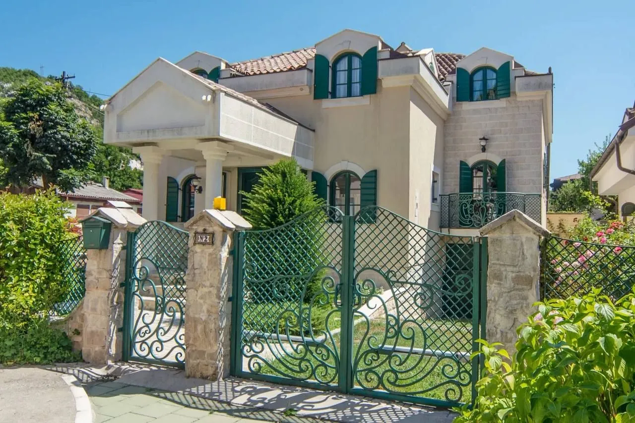 Spoljašnji izgled kuće sa dvorišnijm kapijom i zelenilom.