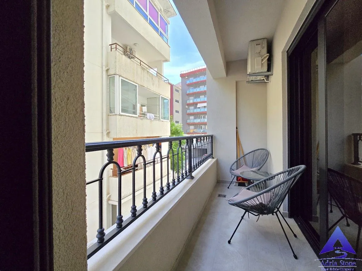 Natkriveni balkon sa stolicama i pogledom na okolne zgrade.