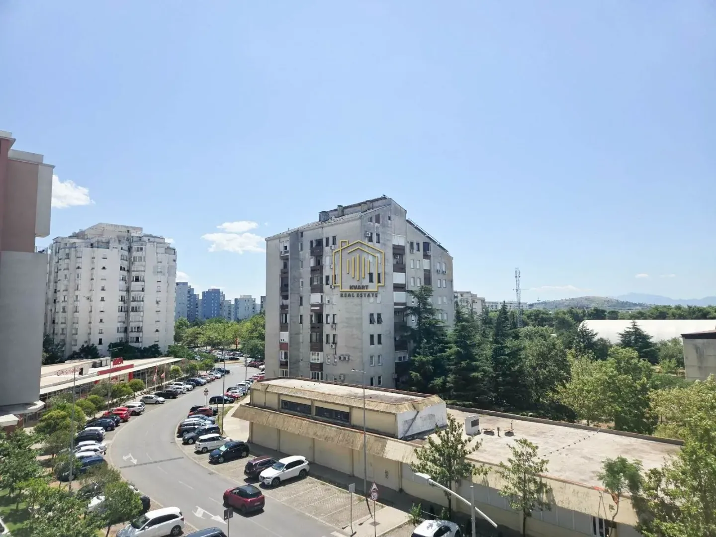 Pogled sa prozora na okolne zgrade i ulicu sa parkingom.