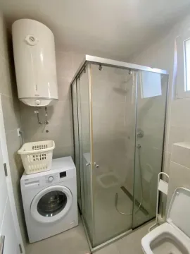 Small bathroom with a shower cabin, washing machine, and water heater. - image 8