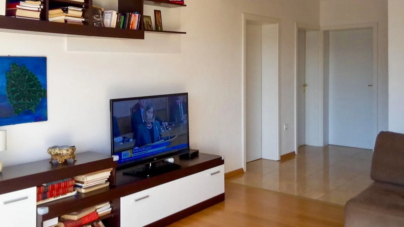 Dnevna soba sa televizorom, komodom i policama na zidu.