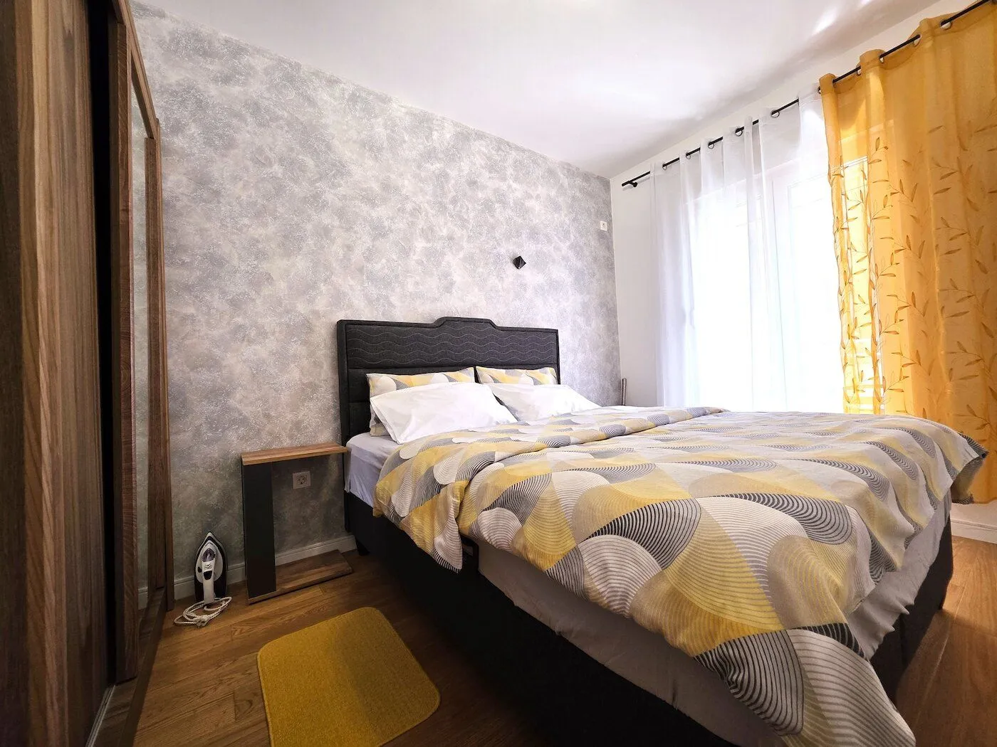 Furnished bedroom with a double bed, wardrobe, and a window with yellow curtains.