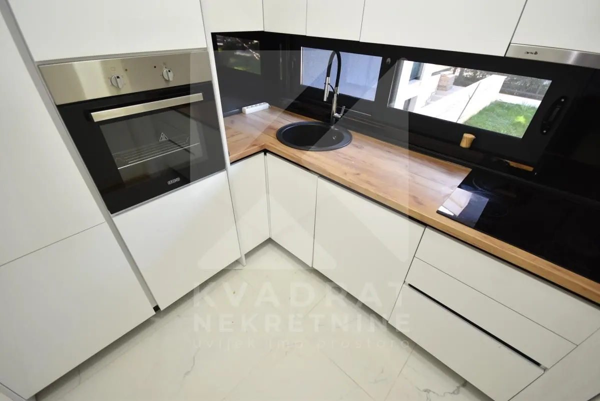 Modern white kitchen with a wooden countertop and built-in appliances.