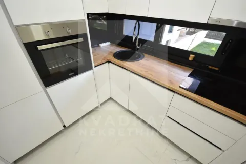 Modern white kitchen with a wooden countertop and built-in appliances. - image 7