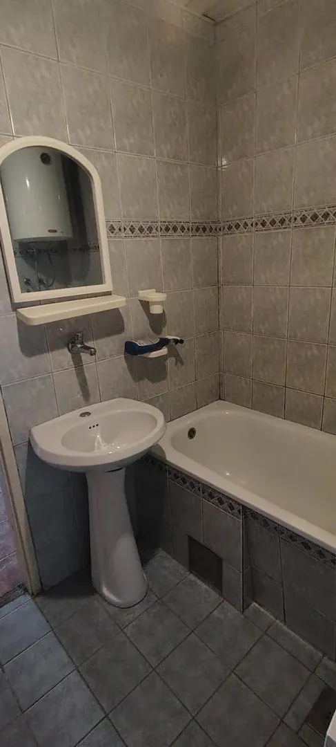 Smaller bathroom with a bathtub, washbasin, and mirror tiled with ceramic tiles.