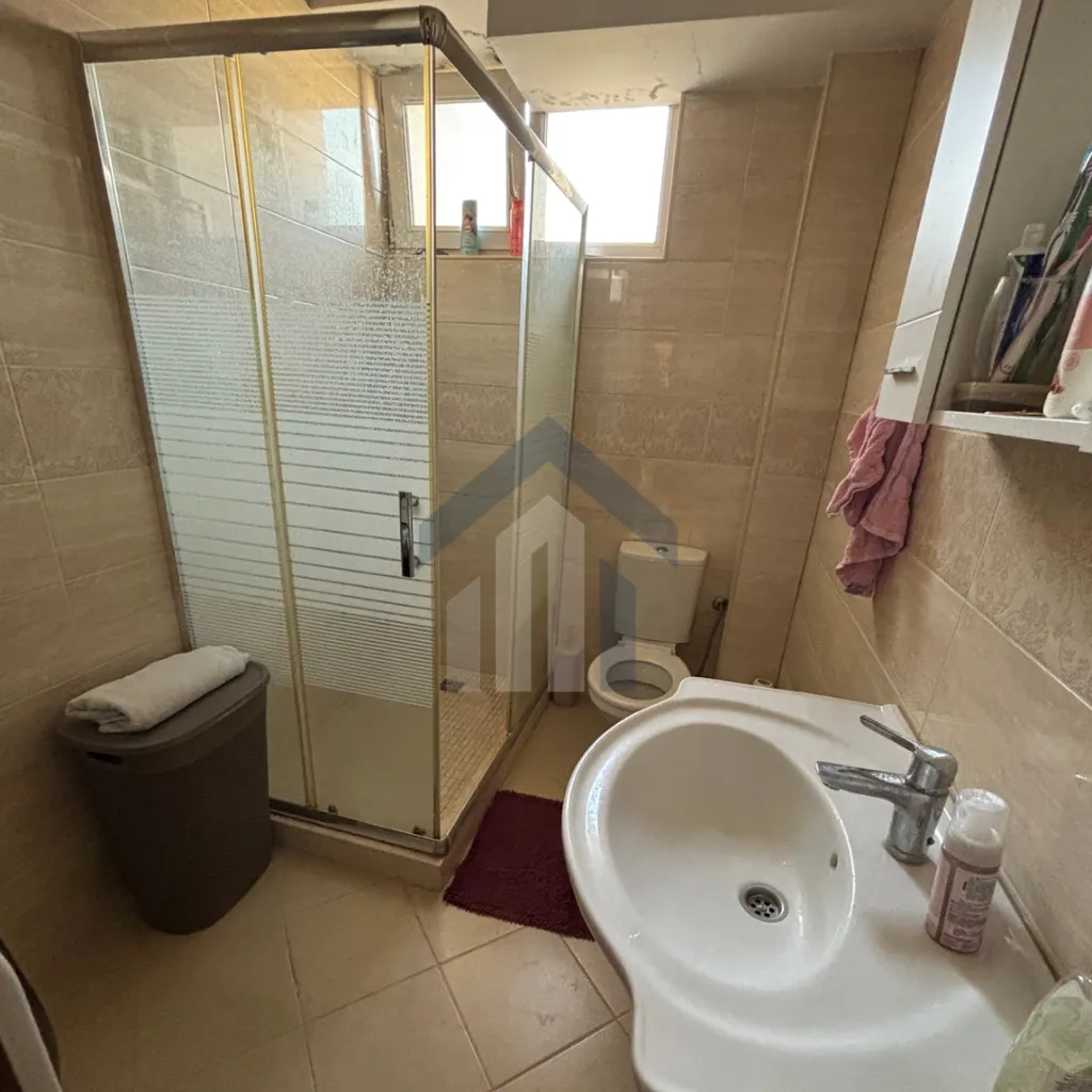 Small bathroom with a shower cabin, washbasin, and toilet in beige tiles.