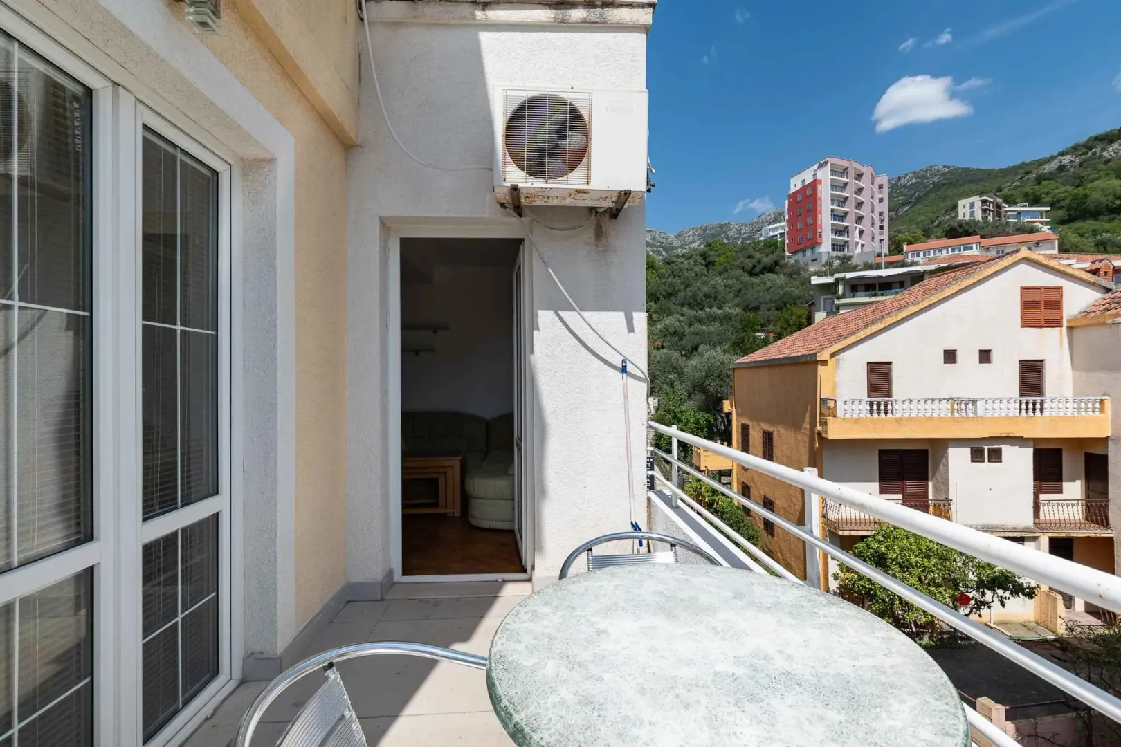 Small furnished balcony with a table and a view of surrounding buildings and hills.