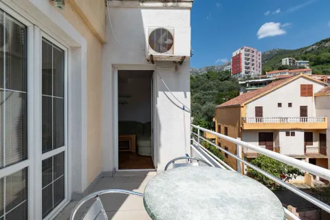 Small furnished balcony with a table and a view of surrounding buildings and hills. - image 10