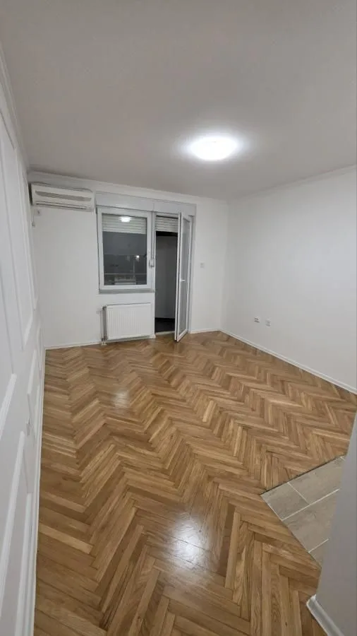 Prazna soba sa parketom i izlazom na balkon.