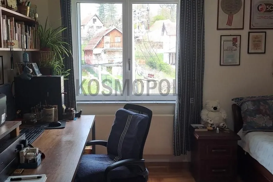 Nameštena spavaća soba sa radnim stolom i prozorom koji gleda na dvorište.