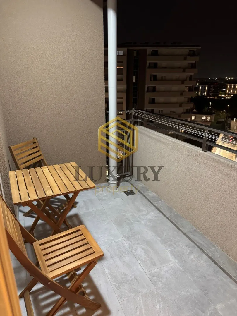 Small balcony with a wooden table and chairs at night.