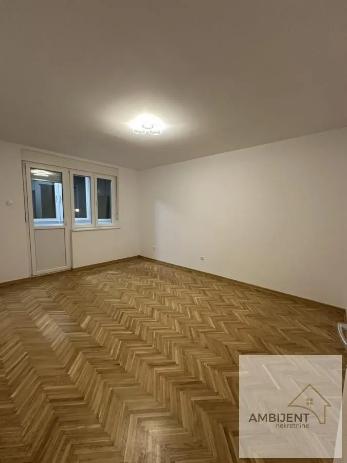 Prazna soba sa parketom i prozorom.
