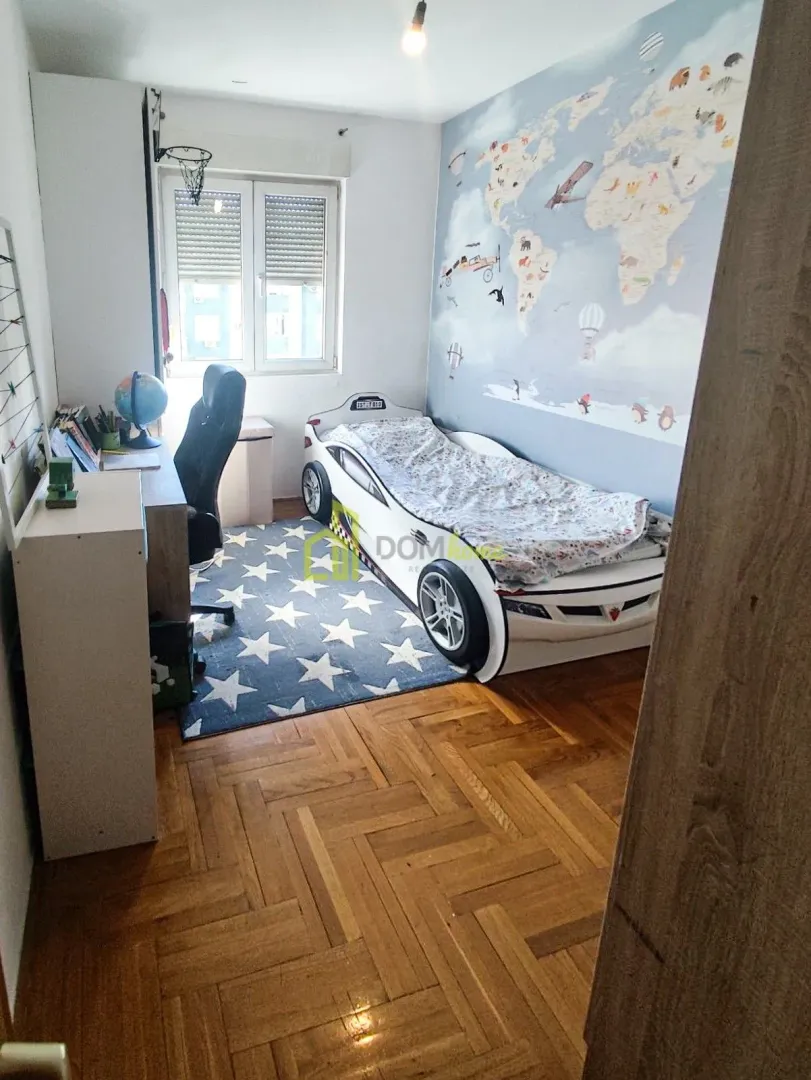 Dječija soba sa krevetom u obliku automobila, radnim stolom i parketom na podu.