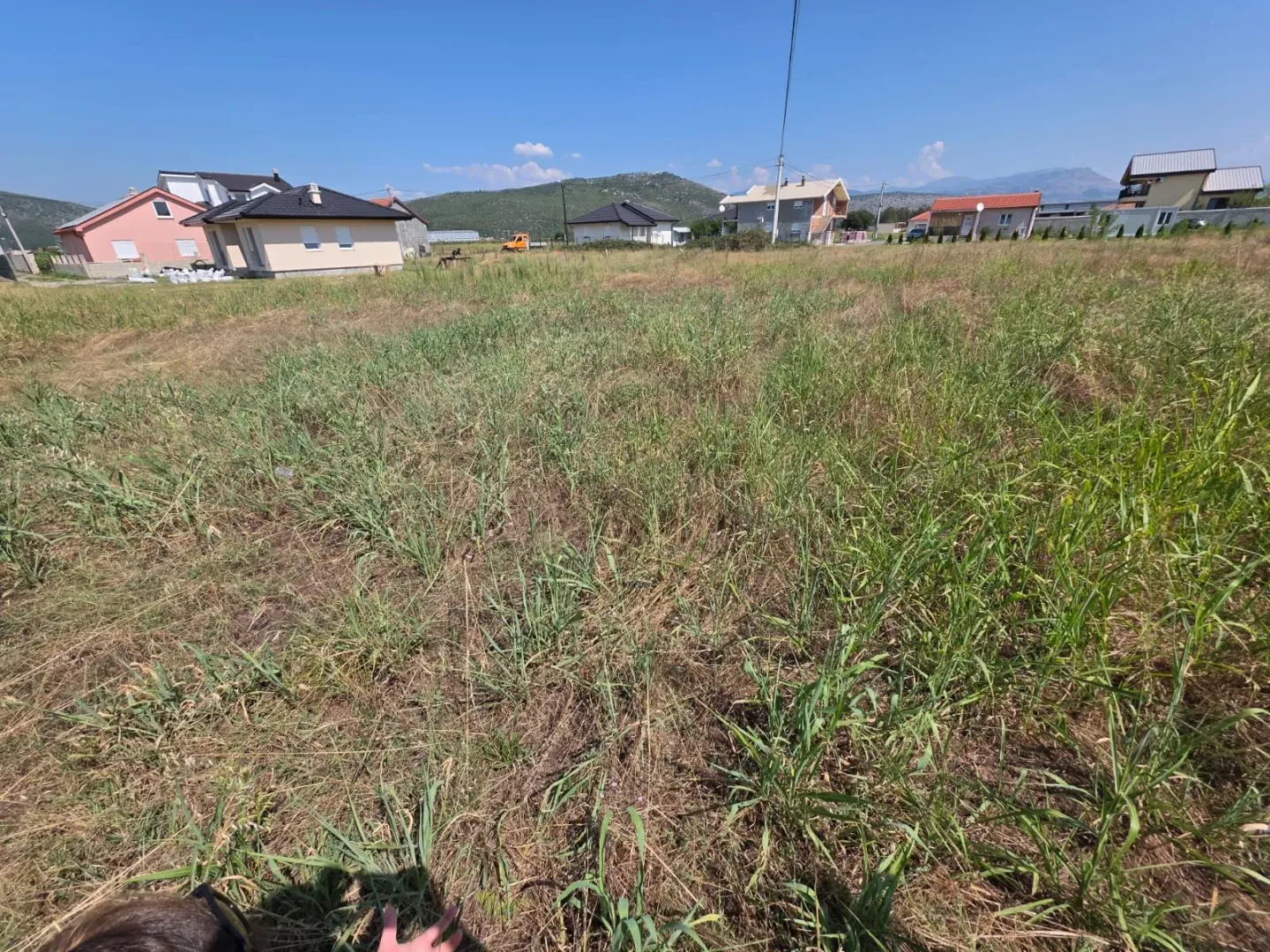 Pogled na prostrani plac sa travom i okolne kuće u pozadini.